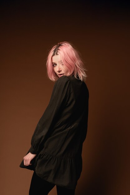 Young woman girl with pink hair at brown wall background studio portrait