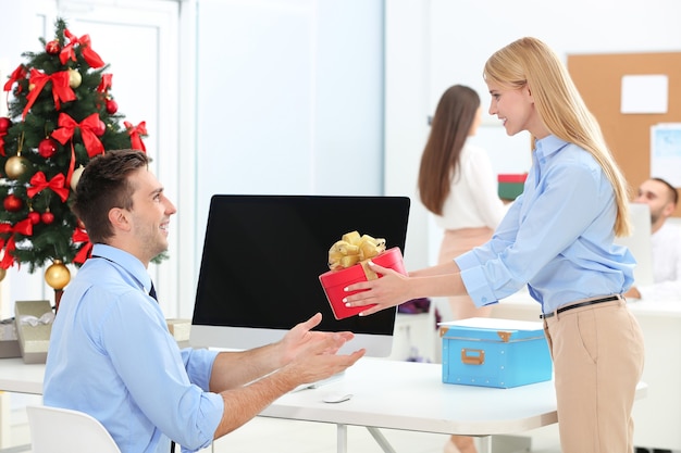 Young woman giving Christmas present to her colleague in office