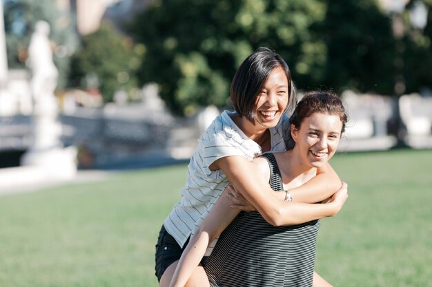 Young woman giving her friend a piggyback ride in the park