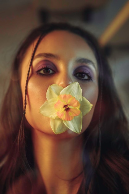 Photo young woman behind a glass wall with a flower in her mouth. creative portrait. high quality photo