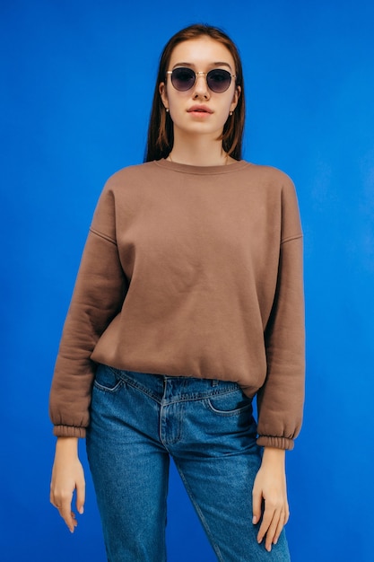 Young woman in glasses and hoodie posing in studio on blue background