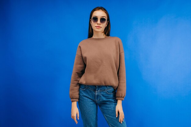 Young woman in glasses and hoodie posing in studio on blue background