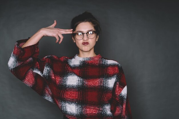 Young woman in glasses making gun gesture near head