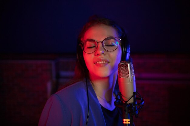 A young woman in glasses singing in neon lighting