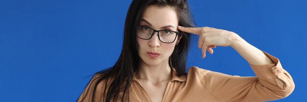 Photo young woman in glasses twirling her finger at temple on blue background