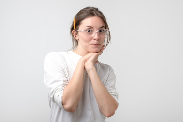 Young woman in glasses with pencil near ear looking at camera