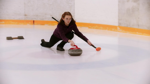 A young woman in glasses with short hair pushes off in the ice field with a granite stone