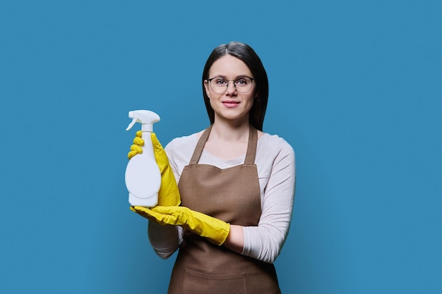 Young woman in gloves apron with organic detergent on blue background