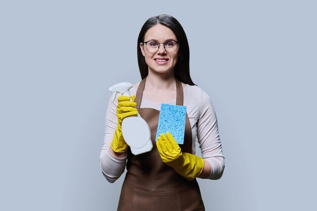 Foto giovane donna con un grembiule a guanti con detergente organico su sfondo grigio