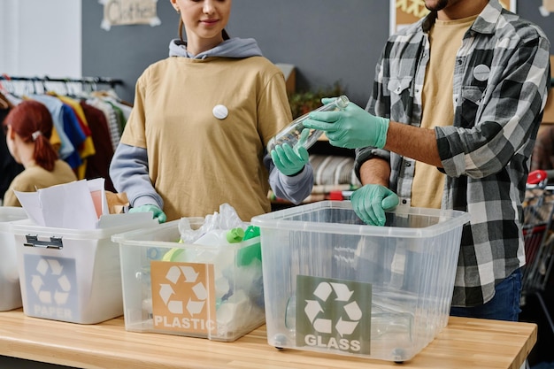 Young woman in gloves passing empty bottle to male volunteer