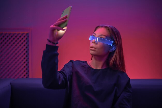 Young woman in glowing glasses uses the phone. 