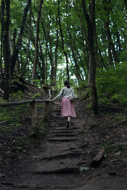 Young woman goes in forest alone. Girl walks in wild park. Back view