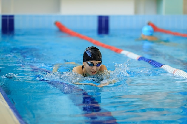 青い水屋内レースプールでゴーグルとキャップ水泳平泳ぎストロークスタイルの若い女性。