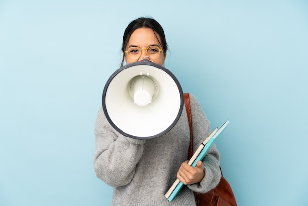 Young woman going to school on blue shouting through a megaphone