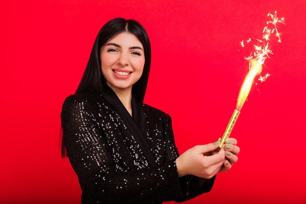 Una giovane donna di buon umore pone con una scintilla in studio un modello su sfondo rosso guarda nella fotocamera