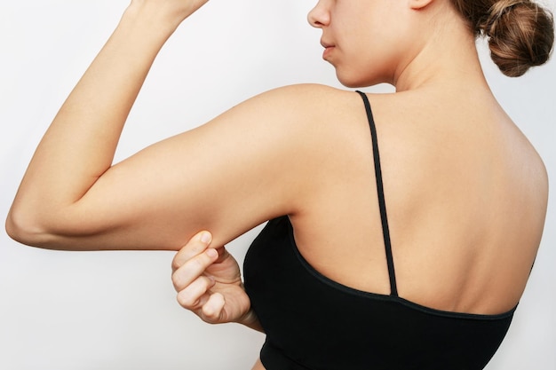Фото Молодая женщина хватается за кожу на плече с лишним жиром, зажимая свободные обвисшие мышцы