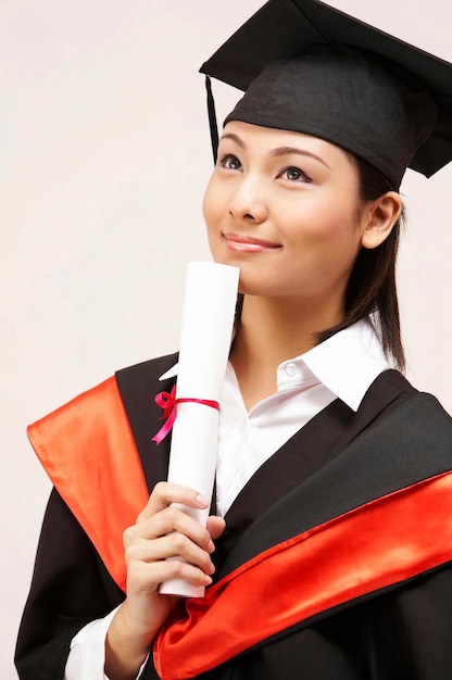 Young woman in graduation gown standing against white background