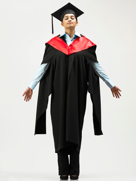 Young woman in graduation gown standing against white background