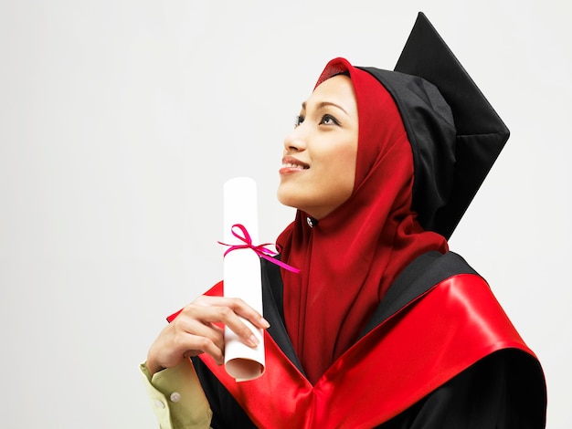 Foto giovane donna in abito da laurea in piedi contro uno sfondo bianco
