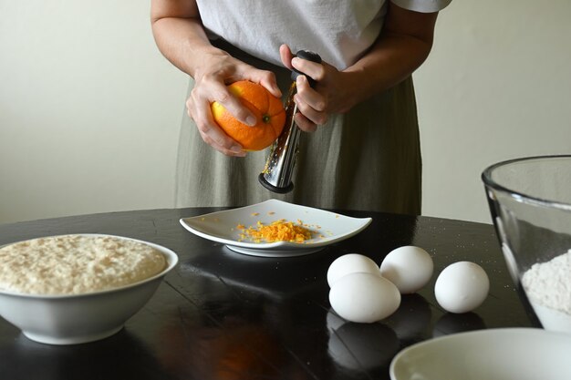 Young woman grating orange surrounded by ingredients