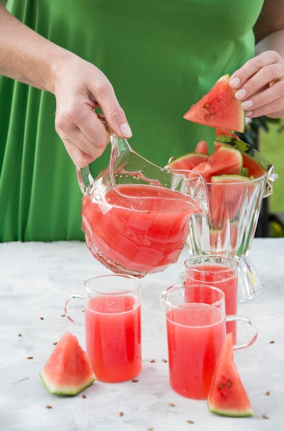 Young woman in a green dress pours a red refreshing drink from watermelon pulp into a glass