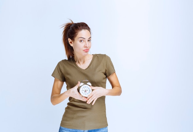 Young woman in green shirt holding an alarm clock