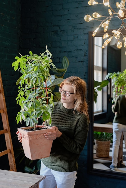 家で植物の世話をしている緑のセーターの若い女性