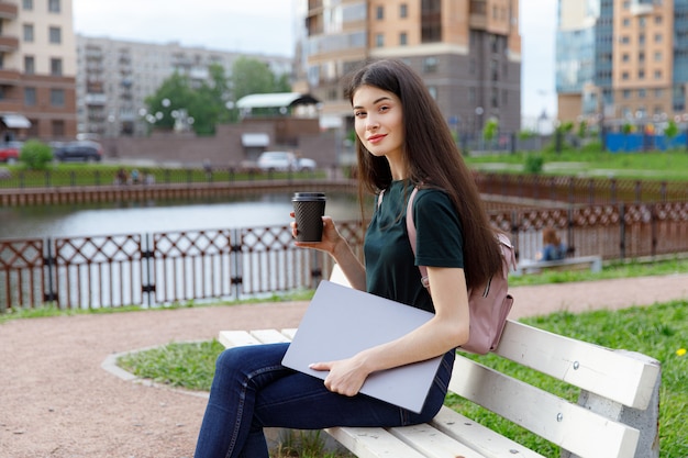 Young woman in a green T-shirt and a backpack sitting on a wooden bench