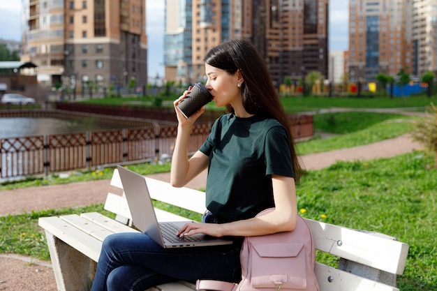 Young woman in a green T-shirt and a backpack sitting on a wooden bench