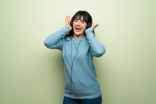 Giovane donna sopra la parete verde che ascolta la musica con le cuffie