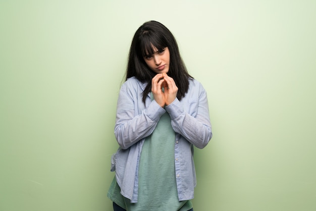 Young woman over green wall scheming something