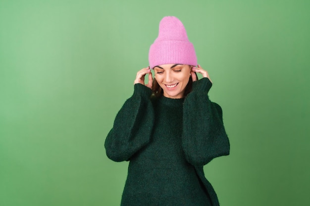 Young woman on green in a warm cozy sweater and a pink hat cute smiling