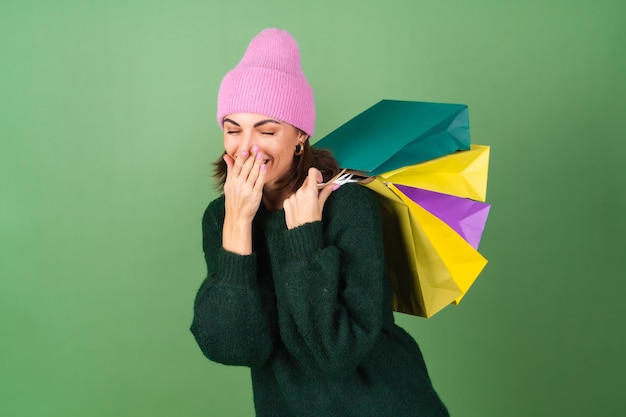 Young woman on green in a warm cozy sweater and a pink hat with colored shopping bags laughs cheerfully