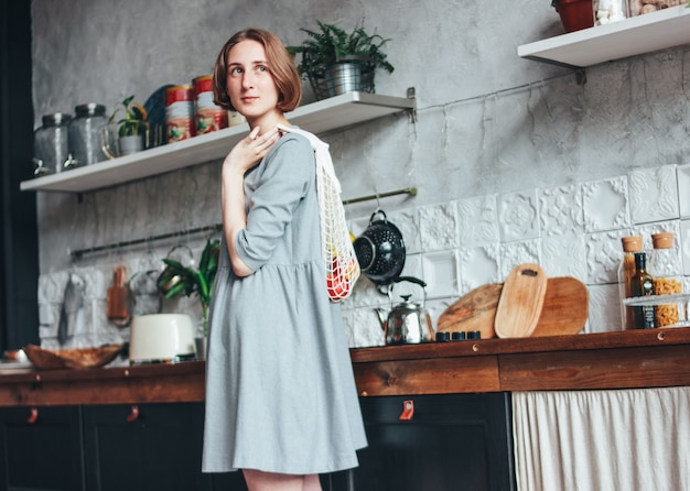 Giovane donna in abito grigio con shopper in maglia borsa sacchetto di tela in cucina