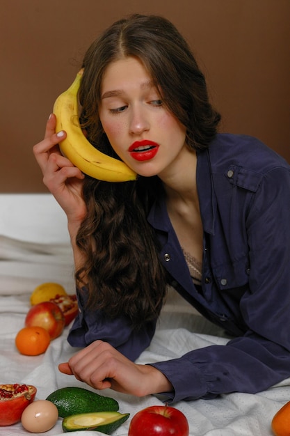 Young woman in group of fruit Healthcare and healthy nutrition concept lies speaks into a banana like a phone