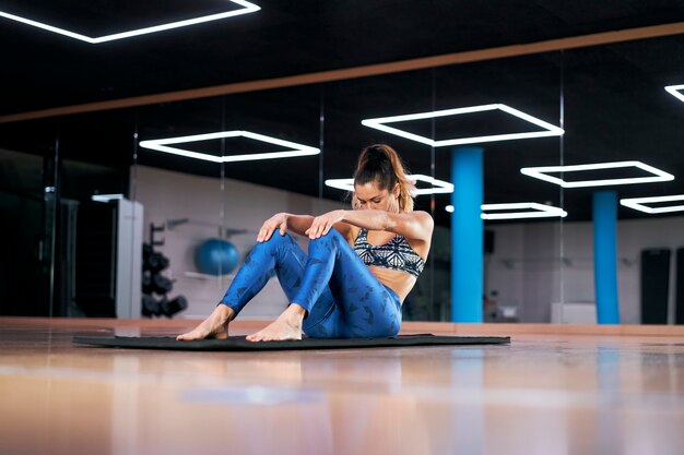 Молодая женщина в тренажерном зале, упражнения в синей спортивной одежде, упражнения на растяжку.