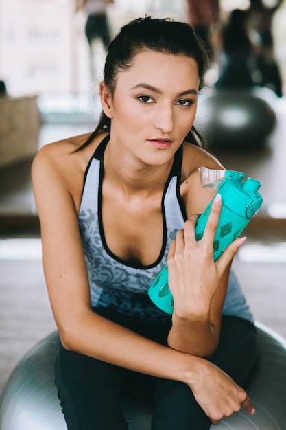 A young woman at the gym sitting on a pilates ball with bottle