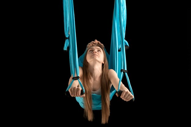 Young woman gymnast hovers in the air in sports hammock Portrait of woman during yoga training on black background