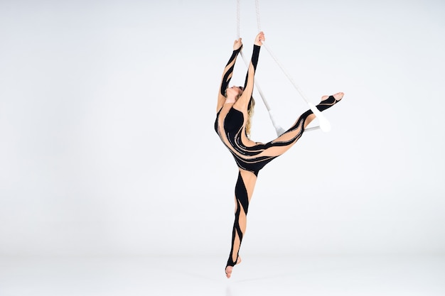 Young woman gymnast wearing black costume on trapeze on white.