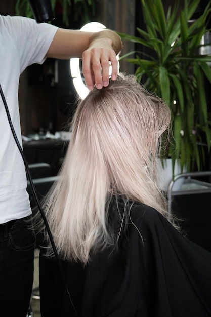 Young woman in a hairdressing salon dyes her hair blond and\
dries hair