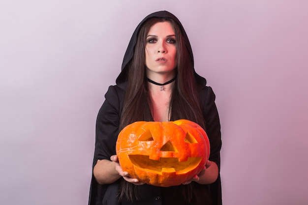 Young woman in Halloween witch costume in studio with yellow pumpkin.