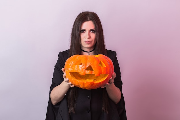 Young woman in halloween witch costume in studio with yellow pumpkin
