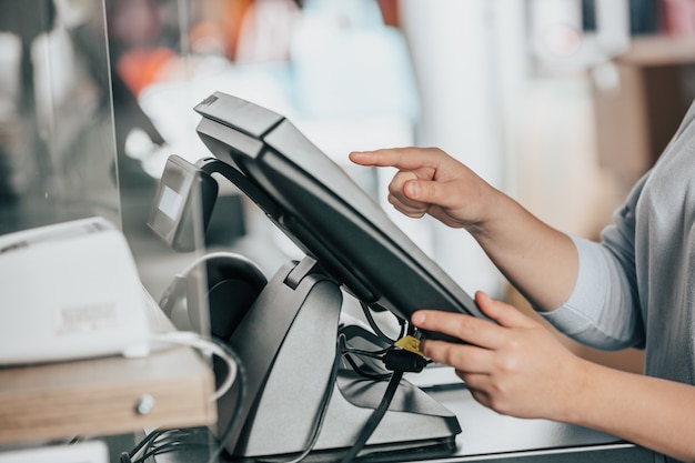 Photo young woman hand charging a payment for a some clothes by touchscreen treasury at huge shopping centre