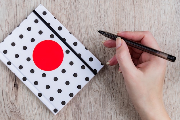 Young woman hand hold black pen and polka dot cover notebook on wooden table