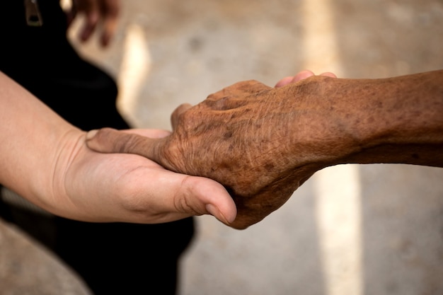 Mano della giovane donna che tiene la mano della persona anziana.