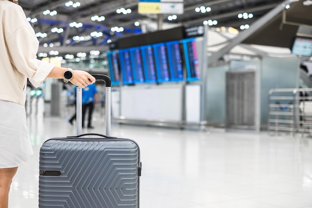 Young woman hand holding luggage handle before checking flight time in airport Transport insurance travel and vacation concepts