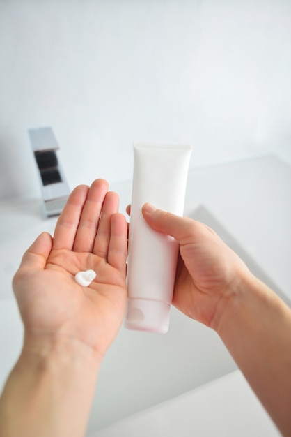 Young woman hand holding and showing white tube and applying cream