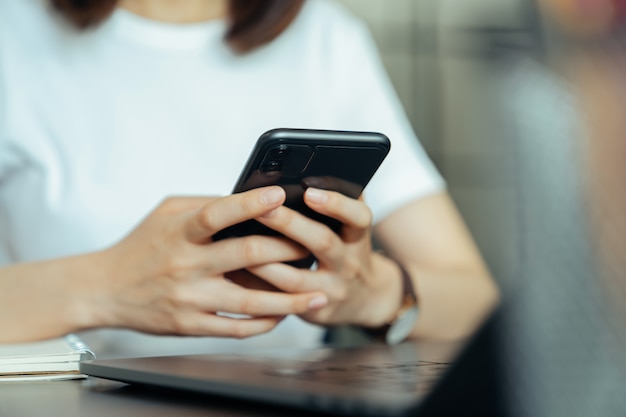 Молодая женщина рука держа смартфон и общаться в чате с друзьями в социальной сети на столе.