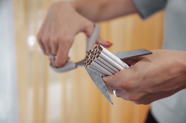 Young woman hands cut cigarettes with scissors. Quit Smok, fight nicotine addiction addicts. Close-up of scissor cutting lot of cigarette. Concept of anti-Smoking and healthy lifestyle. Copy space