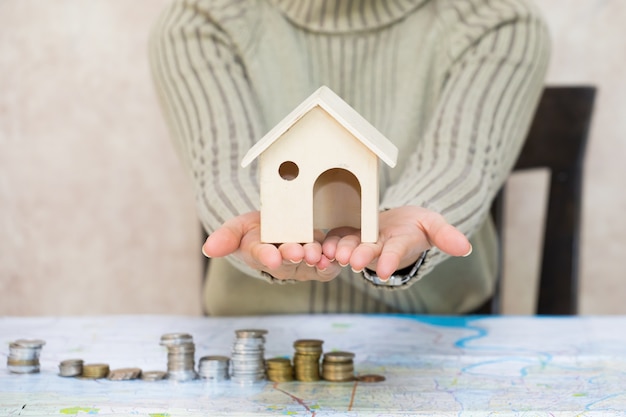 Young woman hands holding house wooden model and coin money map